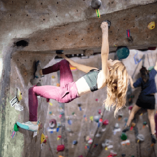 Woman climbing an indoor rock wall, representing audiences interested in outdoor sports, fitness, and active lifestyles.