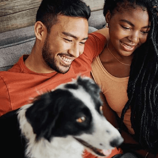 Couple smiling at home with their dog, representing audiences of pet owners and families who value companionship and lifestyle products.