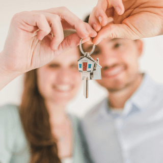 Smiling couple holding a house key, representing audiences of new homeowners, real estate buyers, and families investing in their first property.