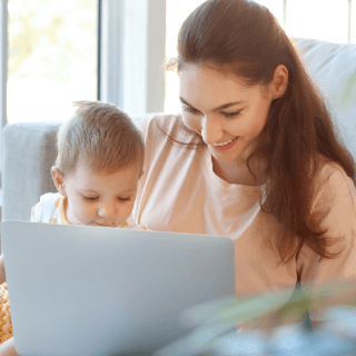 Mother working on a laptop while holding her child, representing audiences of young parents, families, and caregivers interested in home and lifestyle products.