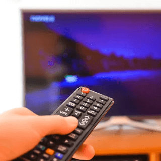 Hand holding a remote control in front of a TV, representing audiences who engage with streaming platforms and connected TV content.